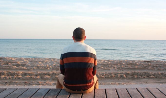 What's up boys Introverti, man sitting on wooden panel facing in the ocean