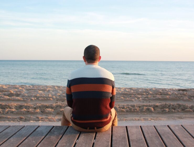 What's up boys Introverti, man sitting on wooden panel facing in the ocean