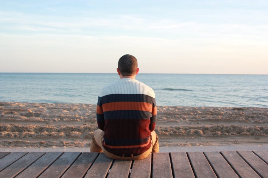 What's up boys Introverti, man sitting on wooden panel facing in the ocean